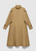 A long camel-colored coat with a loose, A-line silhouette, featuring a high collar, concealed front closure, adjustable cuff straps, and subtle side pockets, displayed against a plain background.
