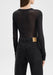 Back view of a model from shoulders to hips, standing upright with arms relaxed at her sides, wearing a sheer black long-sleeve top tucked into high-waisted black jeans against a plain background.
