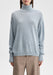 Front-facing mid-length view of a model standing upright with arms relaxed at her sides, wearing a light blue oversized turtleneck sweater paired with beige trousers against a plain background.