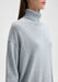 Close-up three-quarter view of the model’s upper body, slightly angled to the side with shoulders turned and head facing forward, highlighting the high turtleneck and relaxed fit of the sweater.