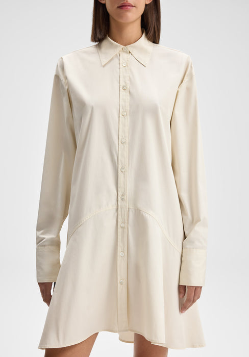 Front-facing view of a model standing upright with arms relaxed at her sides, wearing a cream long-sleeve button-down shirt dress with a pointed collar and softly flared hem against a plain background.