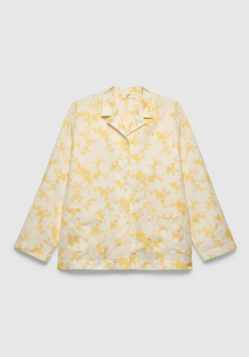 A cream-colored long-sleeve shirt with a relaxed fit, featuring a notched collar, front button closure, patch pockets, and a delicate yellow floral print, displayed against a plain background.