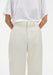 Close-up of cream-colored tailored trousers with a clean waistband and front seam detail, paired with a white top tucked in, highlighting the smooth fabric and structured fit.