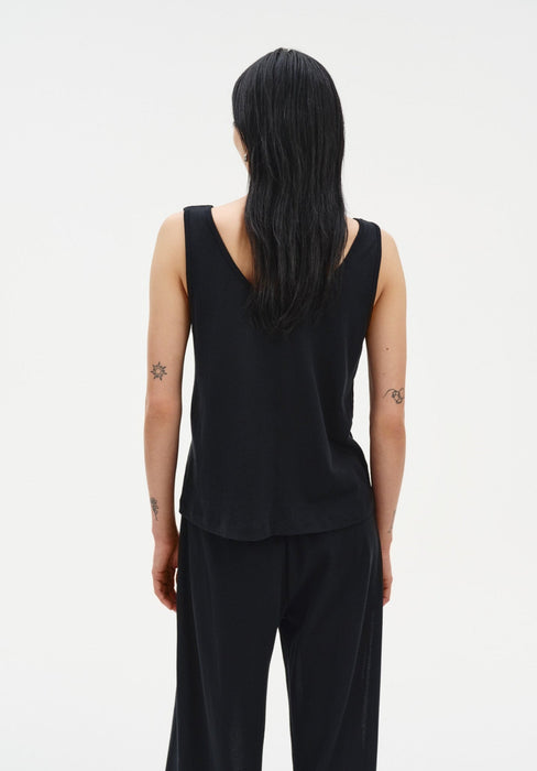 Back view of a woman standing upright with a relaxed posture, arms at her sides, facing away from the camera against a plain studio background.