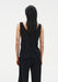 Back view of a woman standing upright with a relaxed posture, arms at her sides, facing away from the camera against a plain studio background.