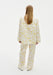 Back view of a model in a cream outfit with yellow abstract floral print, featuring a loose long-sleeve blouse and relaxed straight-leg trousers with a fluid drape.