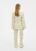 Back view of a model wearing a cream two-piece outfit with a yellow abstract floral print, featuring a long-sleeve tunic top and matching straight-leg trousers.