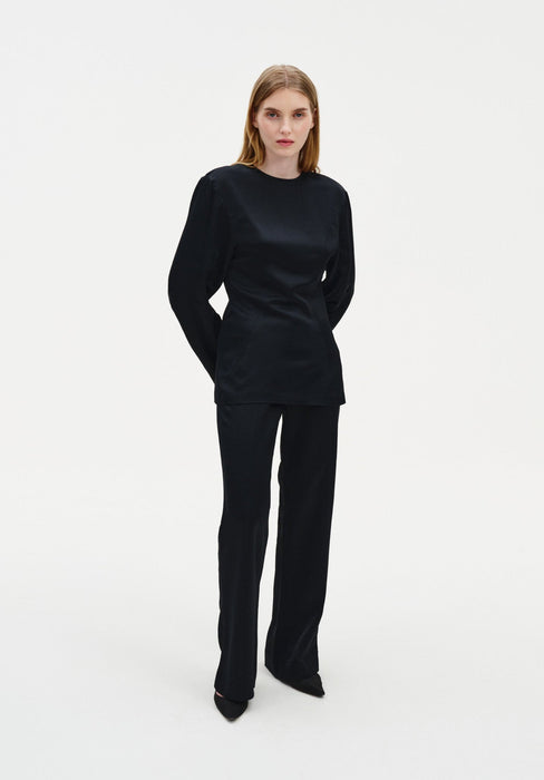 Full-length front view of a woman wearing a black long-sleeve top and matching tailored trousers, showcasing a sleek, fitted silhouette with a smooth finish against a plain studio background.