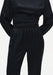 Close-up of a black outfit showing the back waist and upper trousers, featuring a smooth, slightly lustrous fabric, a wide fitted waistband, and softly gathered detailing at the top of the pants.