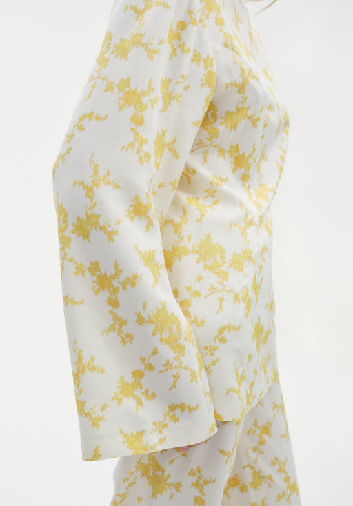 Close-up side view of a cream-colored long-sleeve top with a yellow floral pattern, highlighting the smooth fabric and relaxed fit over matching trousers.