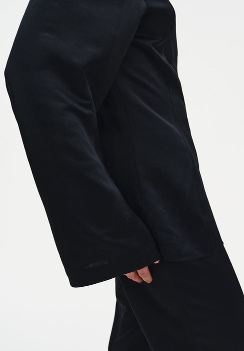 A close-up side view of a person’s arm and torso in a relaxed stance, showing a slightly bent elbow and natural hand position against a plain background.
