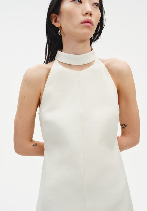 Close-up of a cream sleeveless dress featuring a high choker-style neckline and smooth, structured fabric, shown on a model with delicate drop earrings.