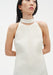 Close-up of a cream sleeveless dress featuring a high choker-style neckline and smooth, structured fabric, shown on a model with delicate drop earrings.
