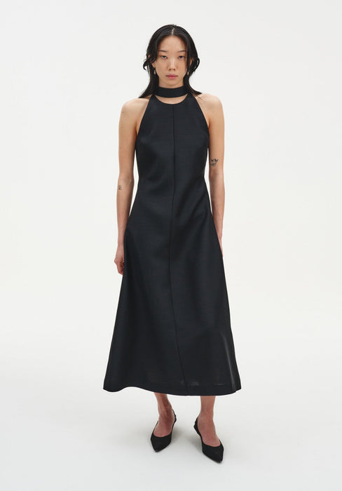 Full-length front view of a model wearing a sleeveless black midi dress with a choker-style neckline and A-line silhouette, paired with black pointed heels.