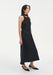 Three-quarter side view of a sleeveless black midi dress with a choker-style neckline and fluid A-line shape, paired with black low heels.