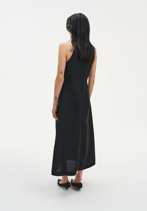 Back view of a sleeveless black midi dress with a clean A-line silhouette, worn with black low heels.