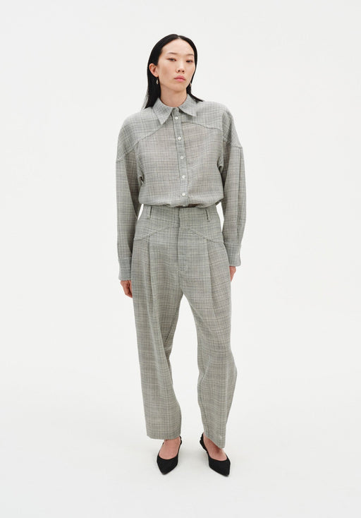 Full-length front view of a woman wearing a grey textured button-up shirt tucked into matching high-waisted trousers with soft pleats, styled with black pointed heels against a minimal white studio background.