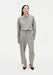 Full-length front view of a woman wearing a grey textured button-up shirt tucked into matching high-waisted trousers with soft pleats, styled with black pointed heels against a minimal white studio background.