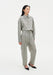 Full-length angled view of a woman wearing a grey textured button-up shirt tucked into matching high-waisted trousers, featuring a relaxed fit and subtle pleats, paired with black pointed heels against a clean studio background.