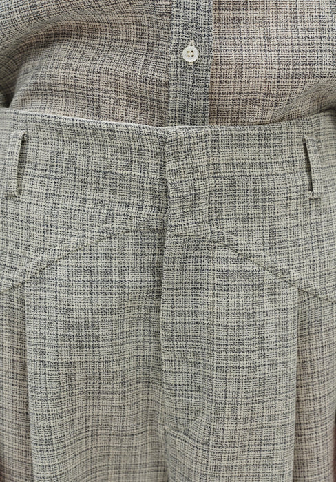 Close-up of grey textured high-waisted trousers showing front pleats, belt loops, and tailored waistband detail.