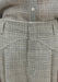 Close-up of grey textured high-waisted trousers showing front pleats, belt loops, and tailored waistband detail.