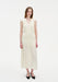 A woman stands facing forward against a plain white background, wearing a sleeveless cream-colored midi dress with a V-neckline and gathered tiered detailing, paired with black pointed heels. Her straight light brown hair is worn down, and she has a neutral expression with arms relaxed at her sides.