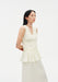 Side view of a model wearing a sleeveless cream blouse with a V-neckline, gathered shirring, and peplum hem, paired with a matching skirt.