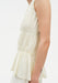 A light cream sleeveless top with gathered, tiered fabric; their arm is visible with small tattoos, and the background is plain and neutral.